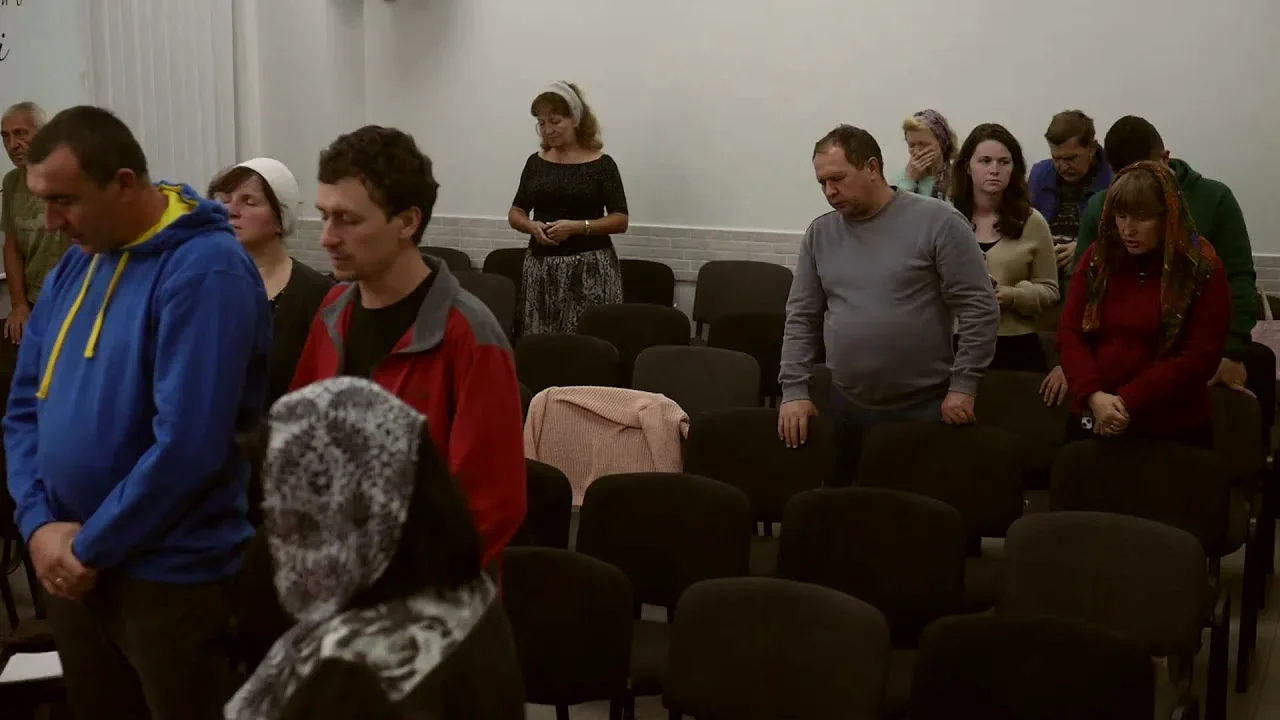 Члени громади стоять між рядами крісел і моляться