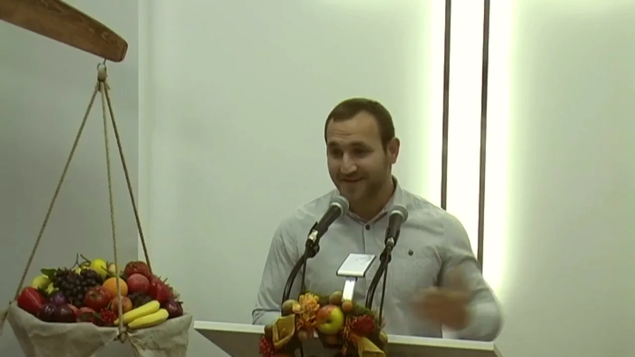 Чоловік говорить біля кафедри, поруч терези й кошик фруктів